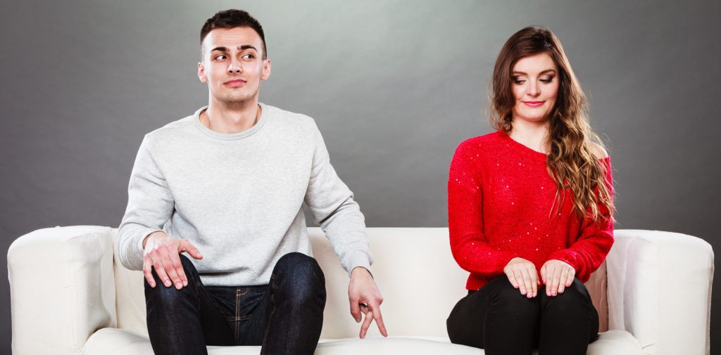 man and woman sitting on a couch together and the man is slowly approaching the woman 