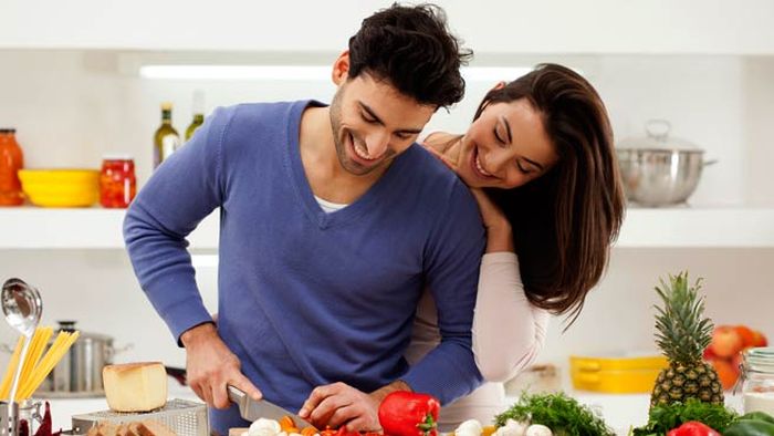 man cooking dinner for a woman and her looking over his shoulder 