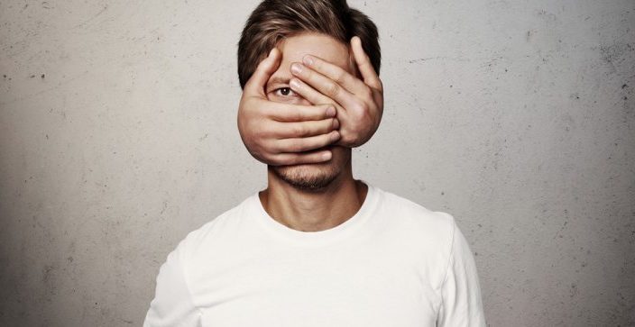 man with hands covering his face except his right eye