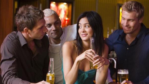 group of men surrounding a woman at the bar